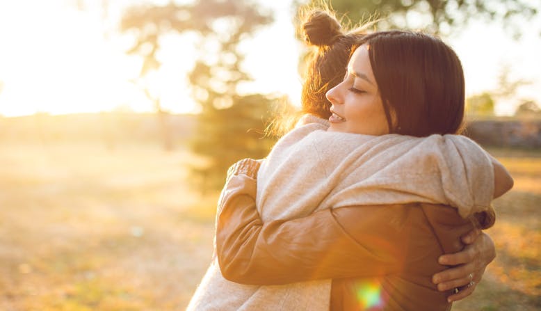 Two women embracing with a sunset behind them.