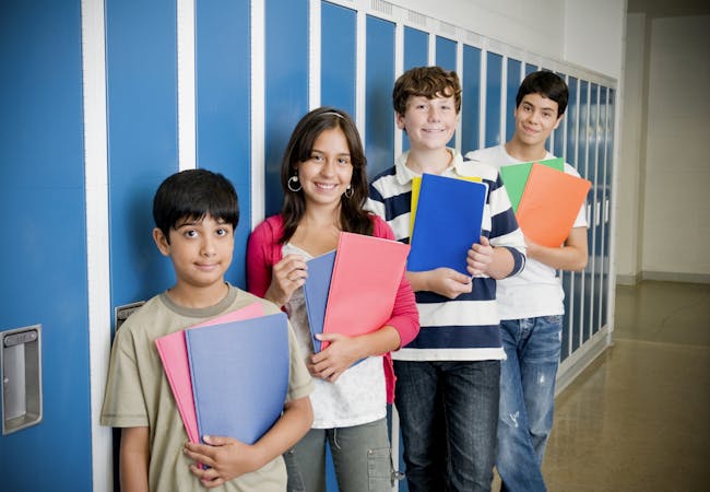 Kids in a school hallway holding folders.