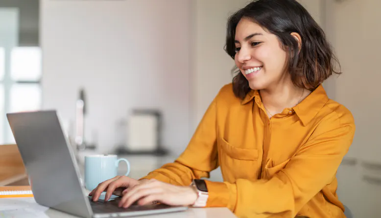 A woman smiling and working on a laptop computer.