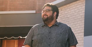 A man stands outside and looks to the side, smiling.