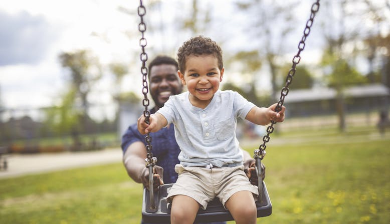A father is pushing his son on a swing in the park.