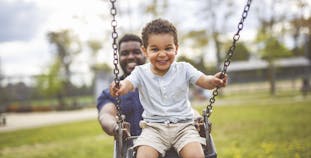 A father is pushing his son on a swing in the park.