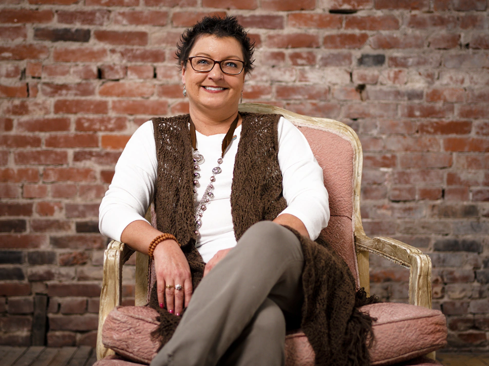 Tami Seretti seated on an armchair with a brick wall in the background.
