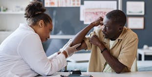 A dermatologist examines a patient's elbow closely.