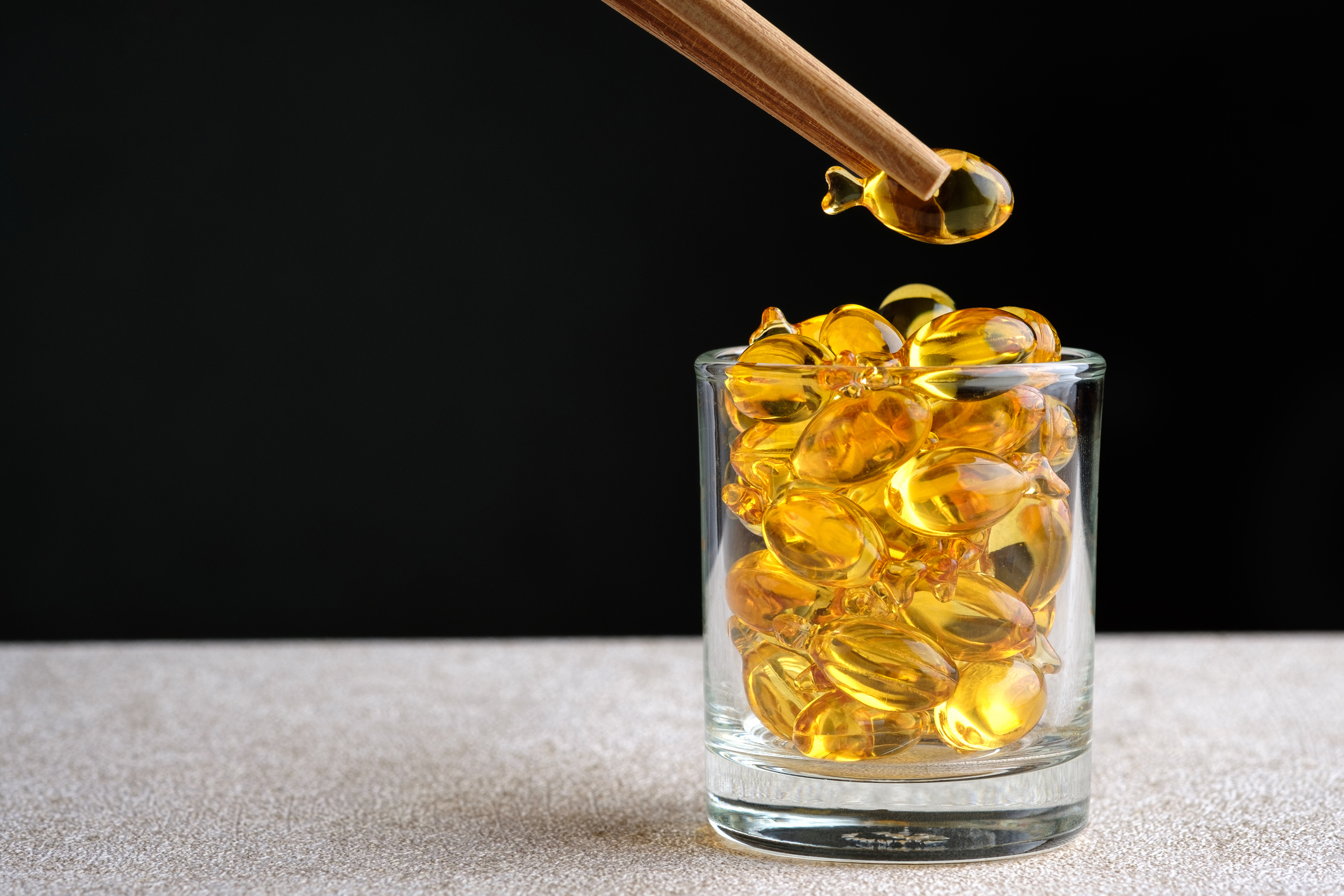 Fish-shaped fish oil supplements in a glass, one is picked up with chopsticks.
