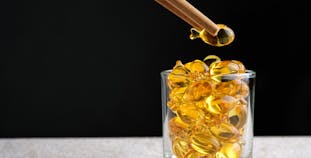 Fish-shaped fish oil supplements in a glass, one is picked up with chopsticks.