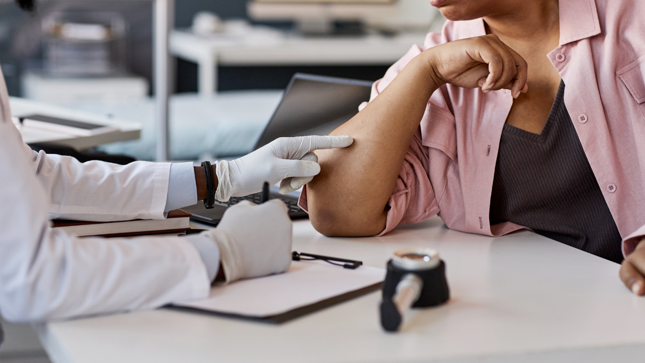 A doctor looks at a patient's skin on their arm.