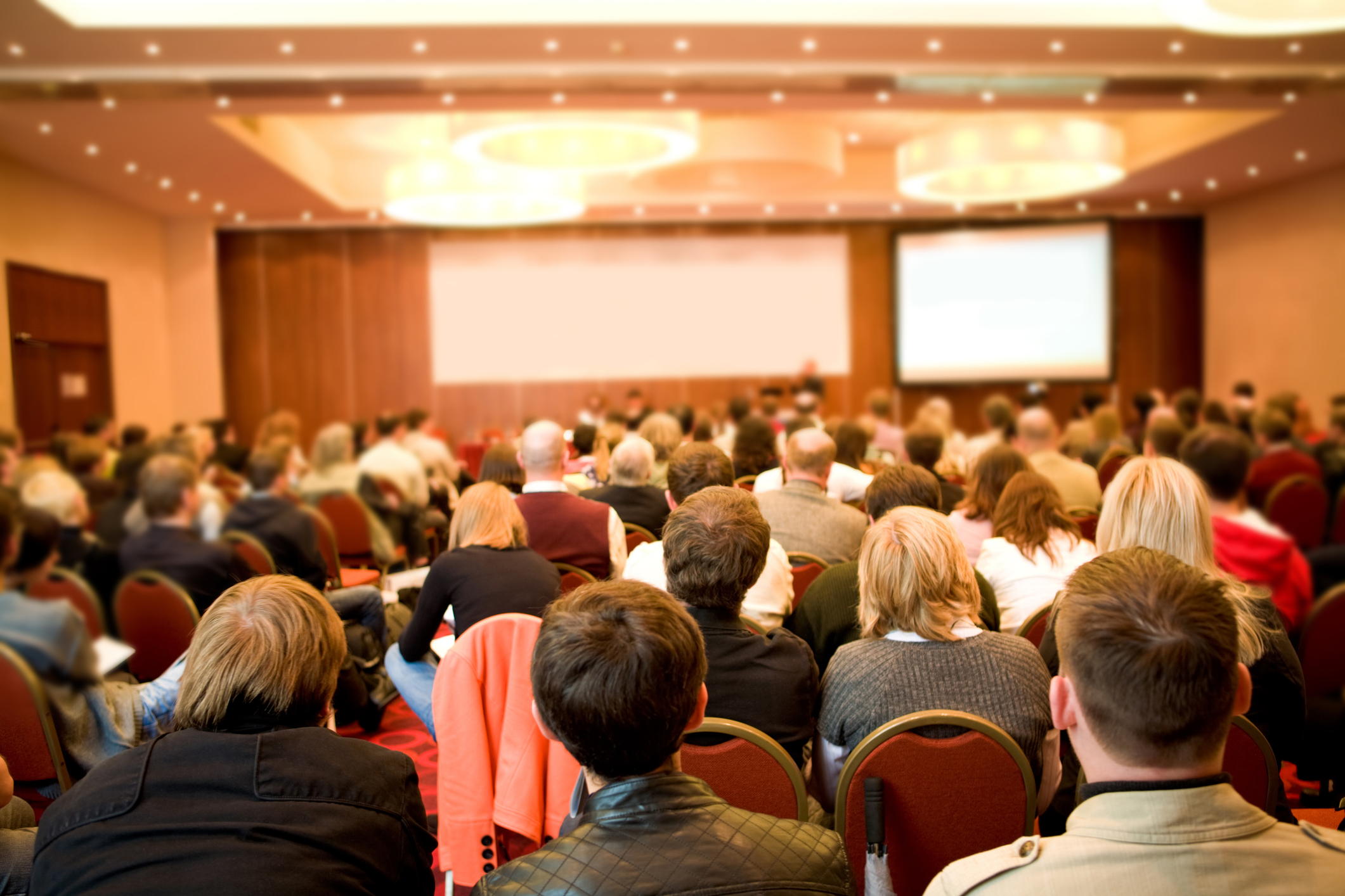 Rear view of many listeners sitting on chairs during a lecture at a conference.