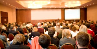 Rear view of many listeners sitting on chairs during a lecture at a conference.