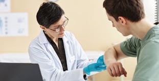 A doctor looks at a patient's skin on their elbow.