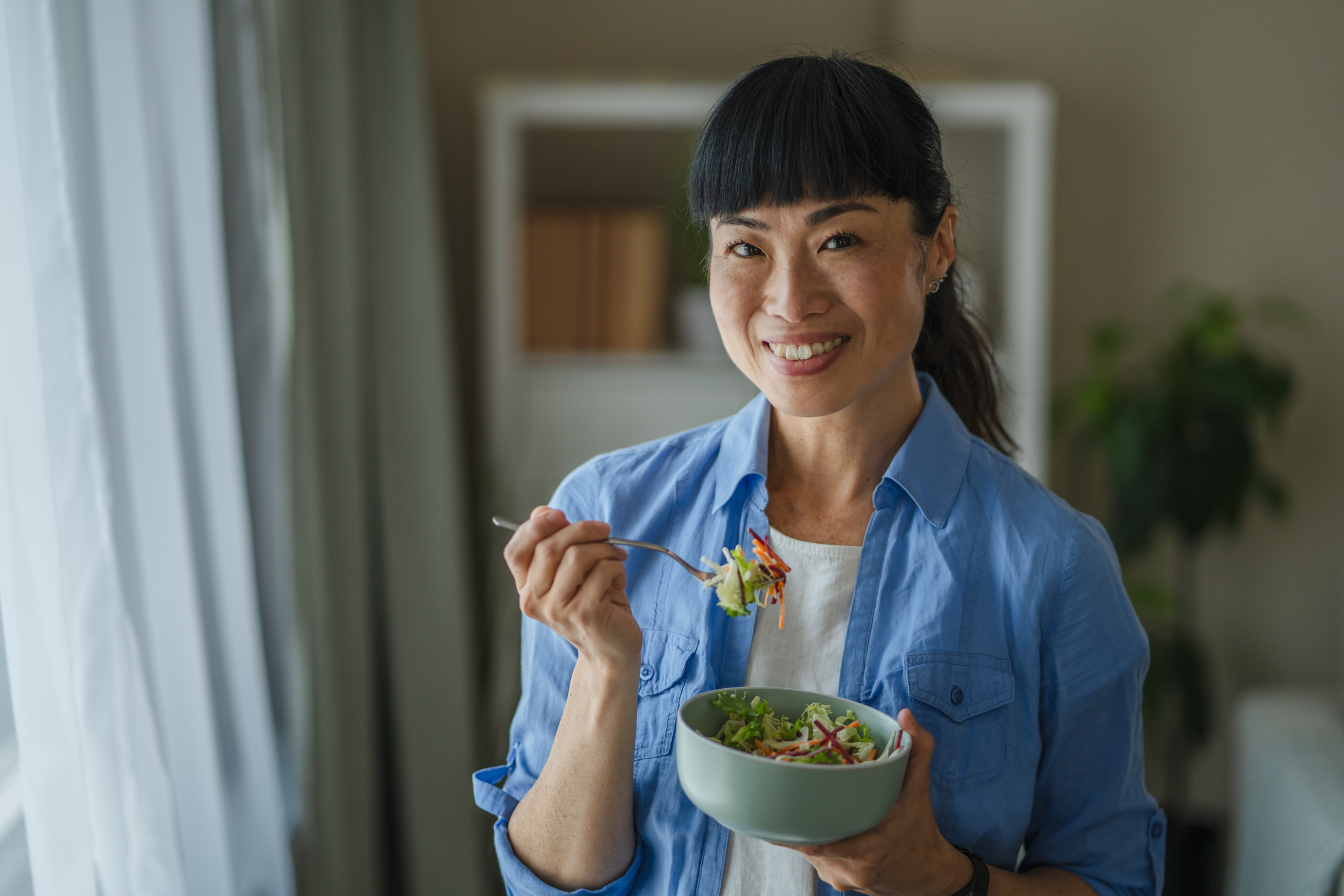 A woman stands and eats a salad.
