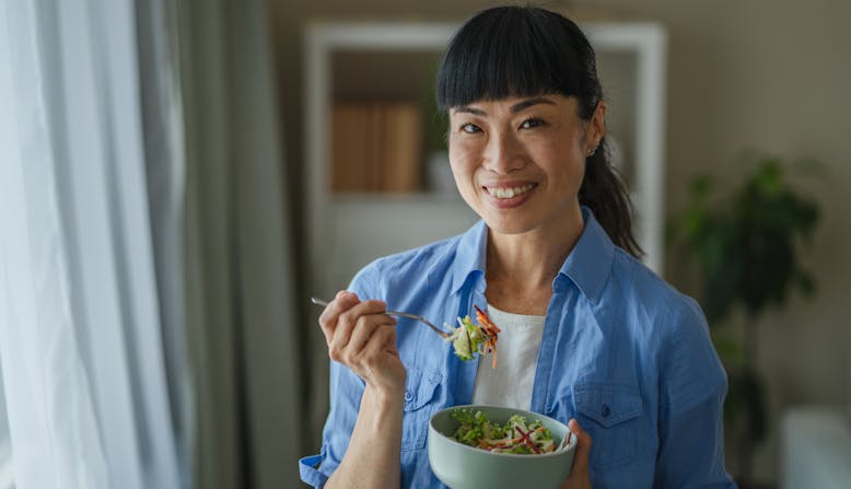 A woman stands and eats a salad.