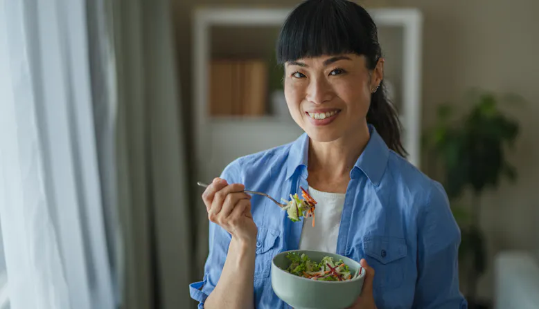 A woman stands and eats a salad.