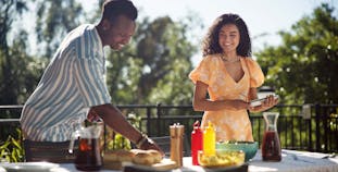 A man and a woman set the table for a meal outside.
