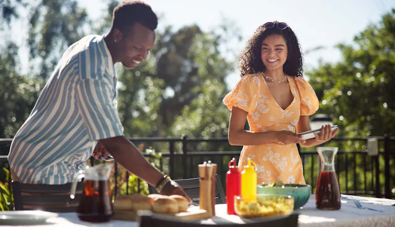 A man and a woman set the table for a meal outside.