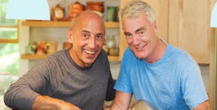 Two older men smiling in a kitchen.