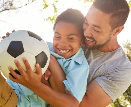 A father and son playing soccer in the park together.