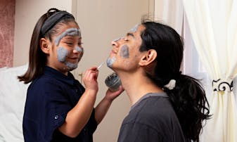 A father and daughter put on face masks together.