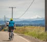 Several people riding bikes away down a street with a mountain in the distance.