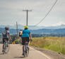 Several people riding bikes away down a street with a mountain in the distance.