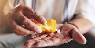 A person pouring pills into their hand from a prescription bottle.