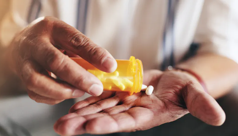 A person pouring pills into their hand from a prescription bottle.