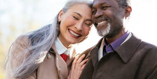 Elderly Asian woman and Black man embracing and smiling outside.