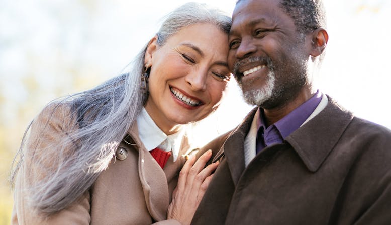 Elderly Asian woman and Black man embracing and smiling outside.