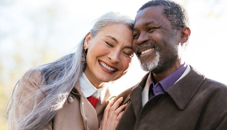 Elderly Asian woman and Black man embracing and smiling outside.