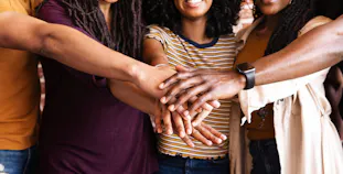 A group of people with skin of color holding their hands in together and smiling.