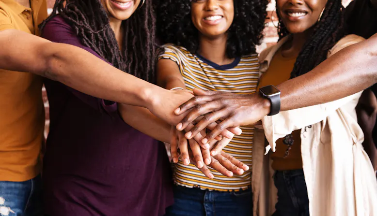 A group of people with skin of color holding their hands in together and smiling.