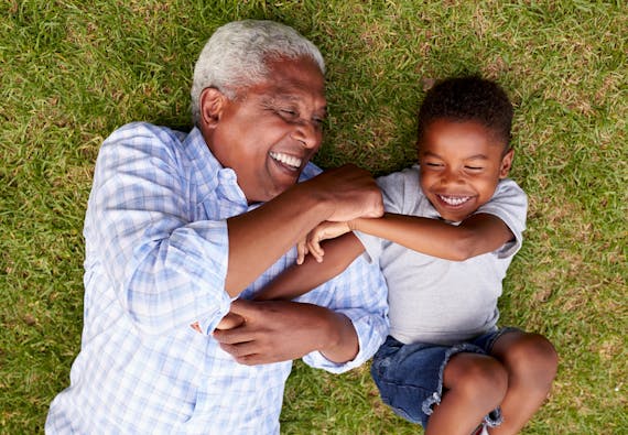 A grandpa and grandson laugh while laying in the grass