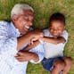 A grandpa and grandson laugh while laying in the grass