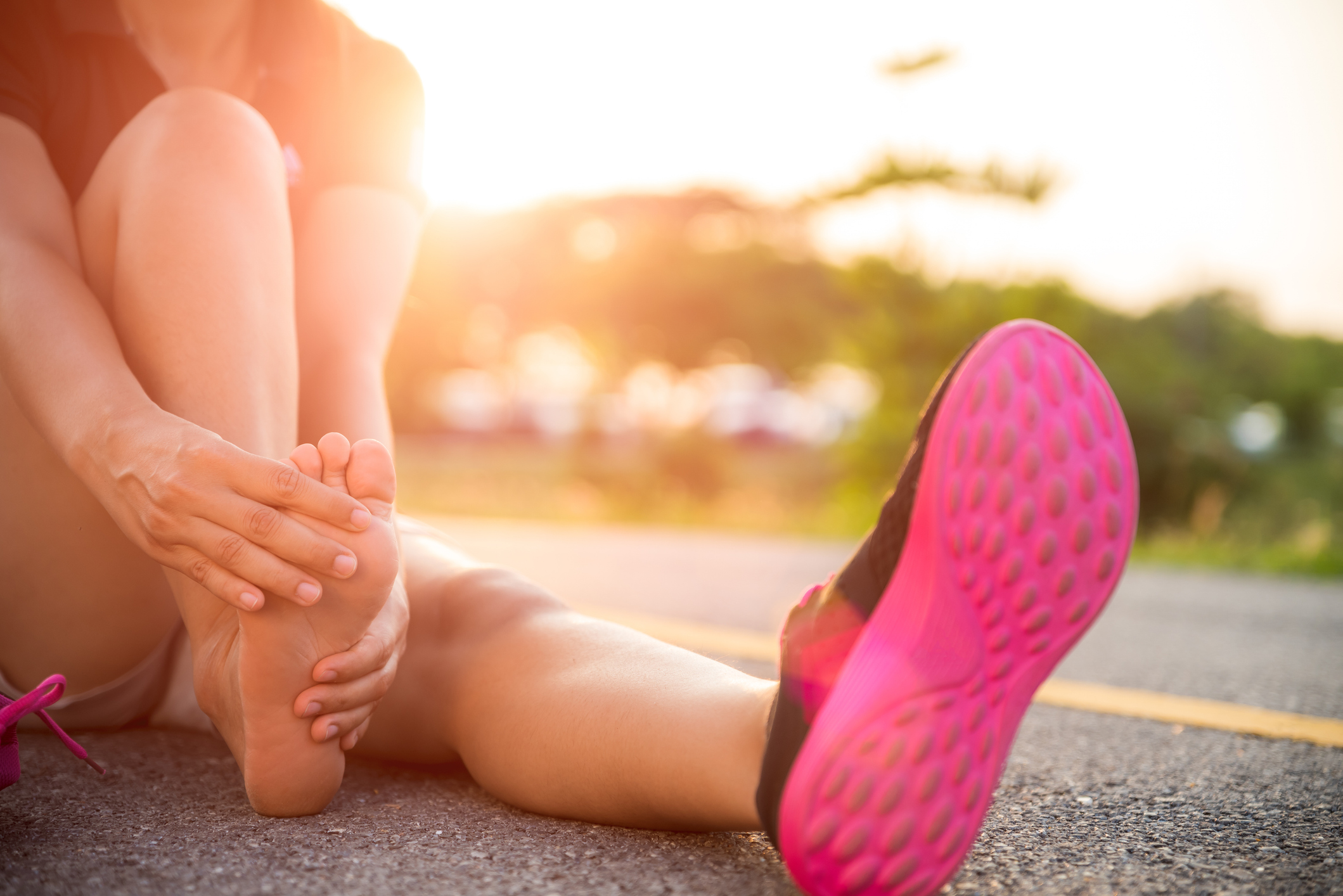 A runner sits on the ground and touches their bare foot.