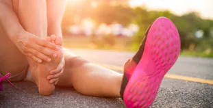 A runner sits on the ground and touches their bare foot.