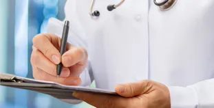 A doctor holds a pen over a clipboard.