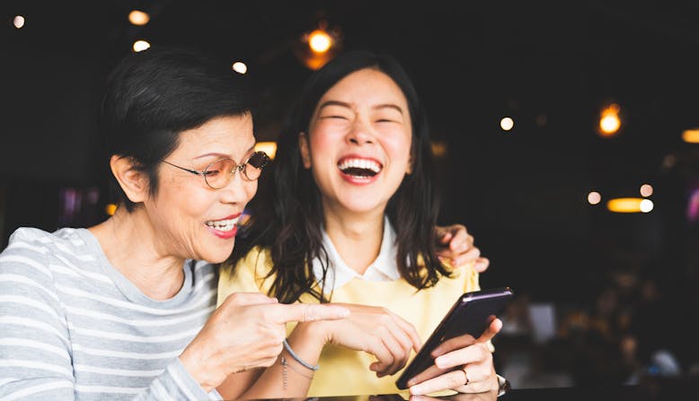 A mother and daughter laugh together as they look at the daughter's phone.