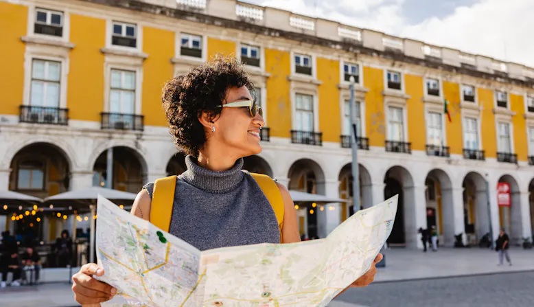 A woman looks at a paper map in a city on vacation.