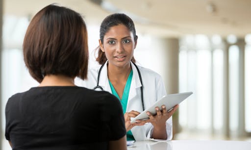 A doctor speaks to a patient with a tablet in her hand.