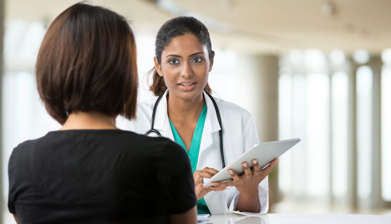 A doctor speaks to a patient with a tablet in her hand.