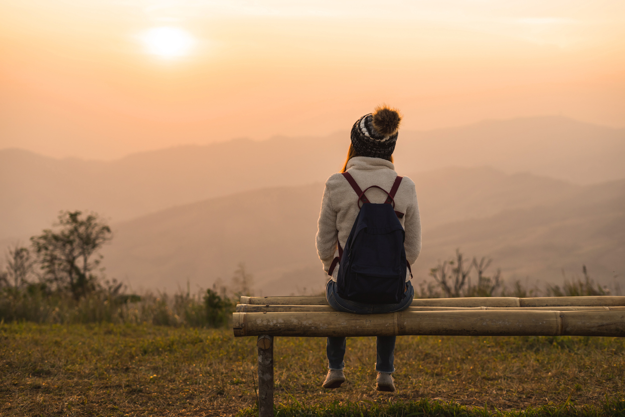 A woman sits on a bench on a hill overlooking mountains.