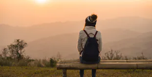 A woman sits on a bench on a hill overlooking mountains.