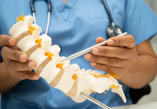 A doctor holds a model of a spine.