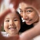 An adult and child smile while making the shape of a heart with their hands.