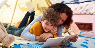 A mother and child lay in a tent and read a book together.