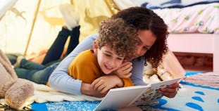 A mother and child lay in a tent and read a book together. 