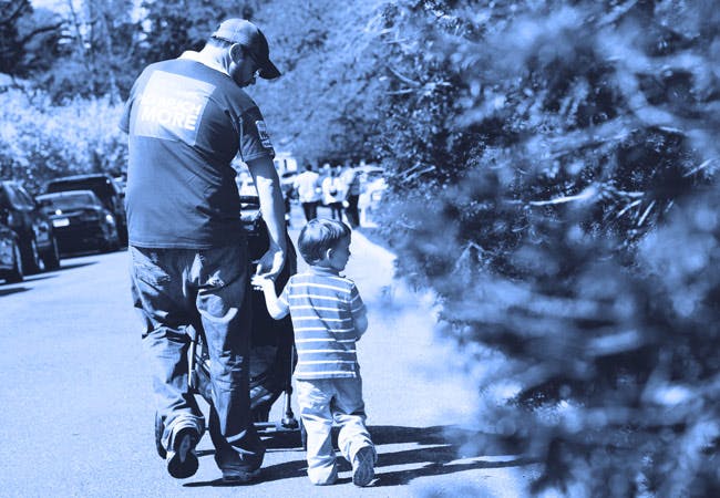 A father and son walk down the street with a baby stoller.
