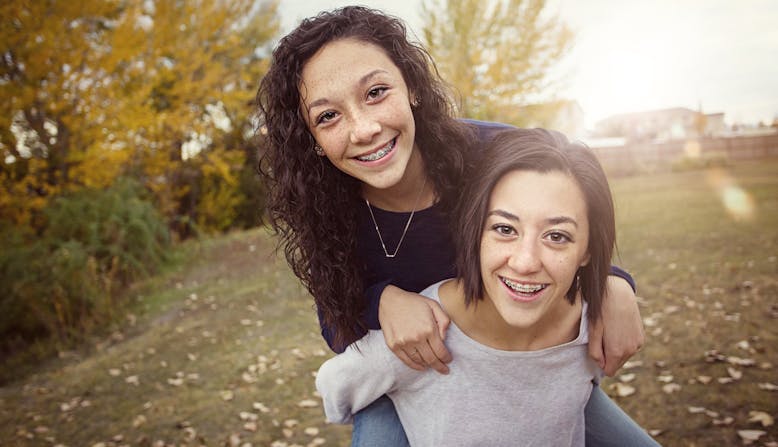 A girl with braces riding piggy back on her twin sister.