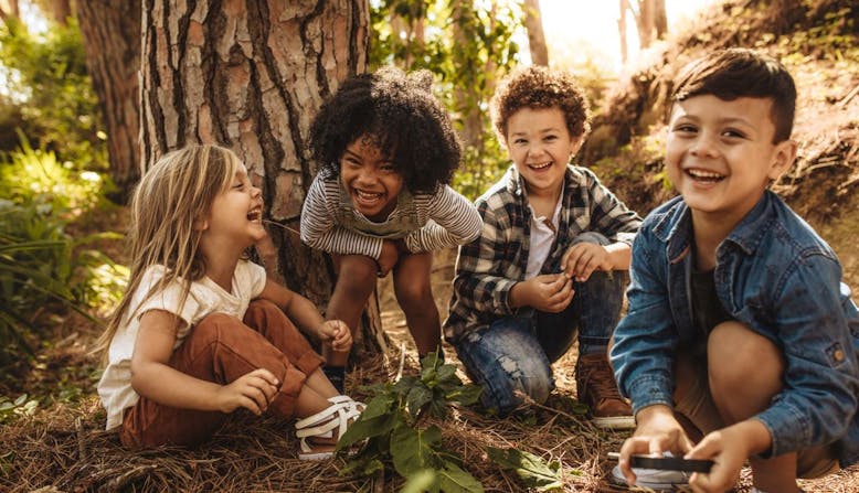 Four kids sitting outside near a tree laughing and smiling.