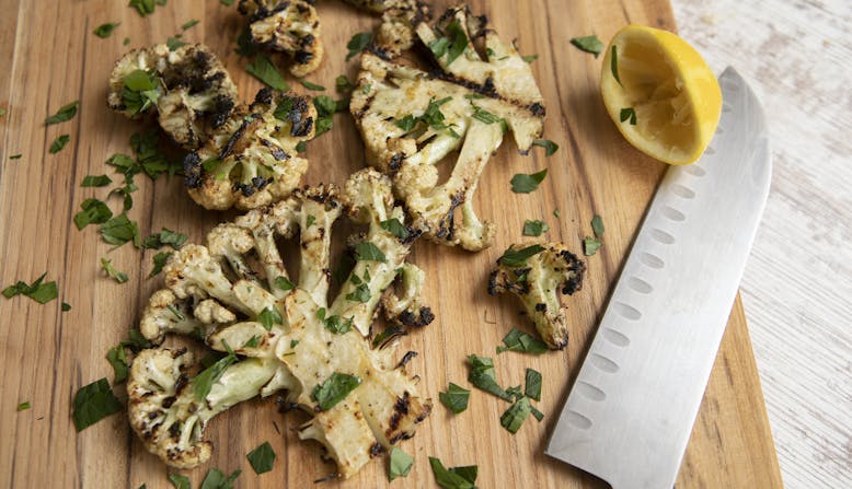 A cutting board with seasoned cauliflower and knife.
